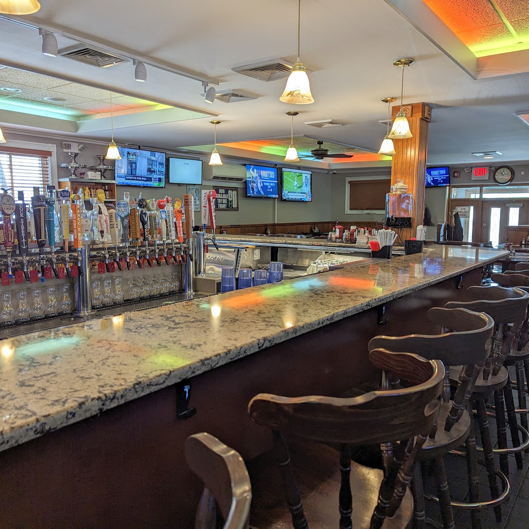 A bar with stools and televisions.